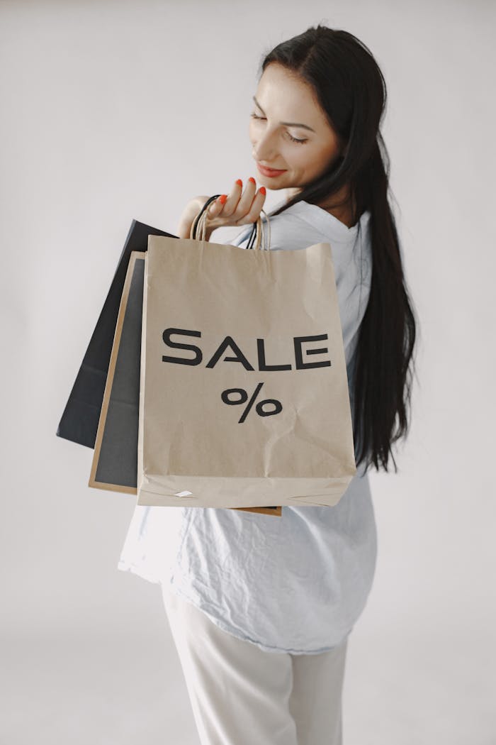 Smiling woman holding shopping bags marked SALE against a white background.
